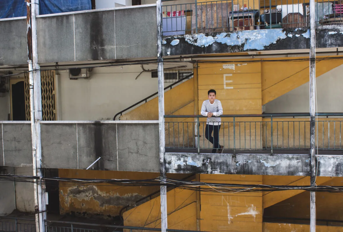 Tyler La on a balcony of a weathered apartment building in Saigon, Vietnam, surrounded by concrete and utility wires