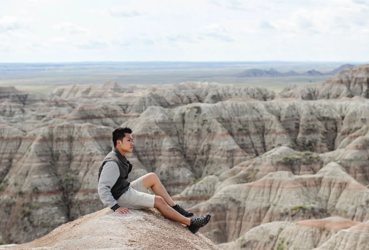 Tyler La sitting on a rocky outcrop at Badlands National Park, gazing across the eroded canyon landscape in South Dakota